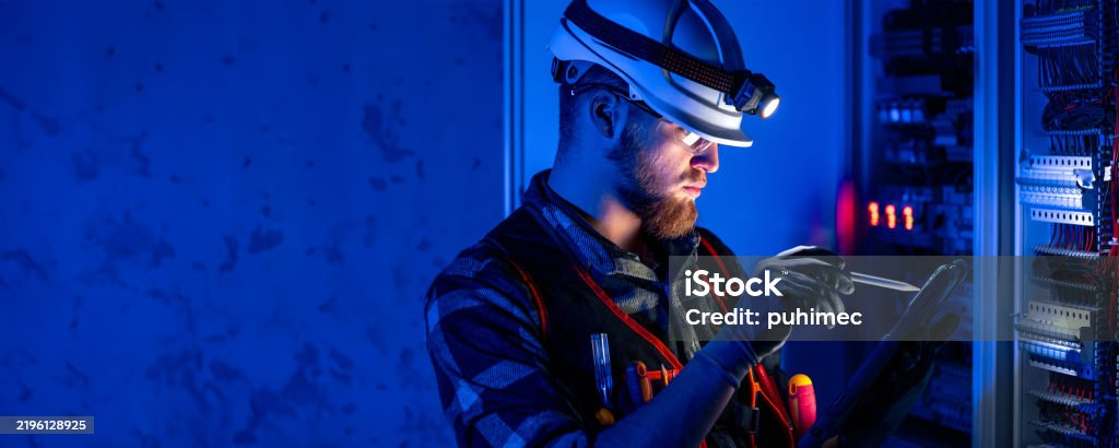 Elektriker mit Stirnlampe prüft eine Schaltanlage