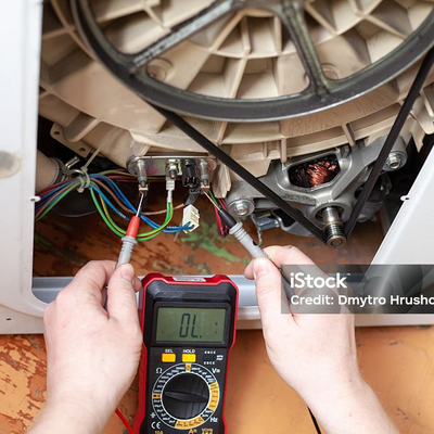 Zwei Hände messen mit einem Multimeter an einer geöffneten Waschmaschine